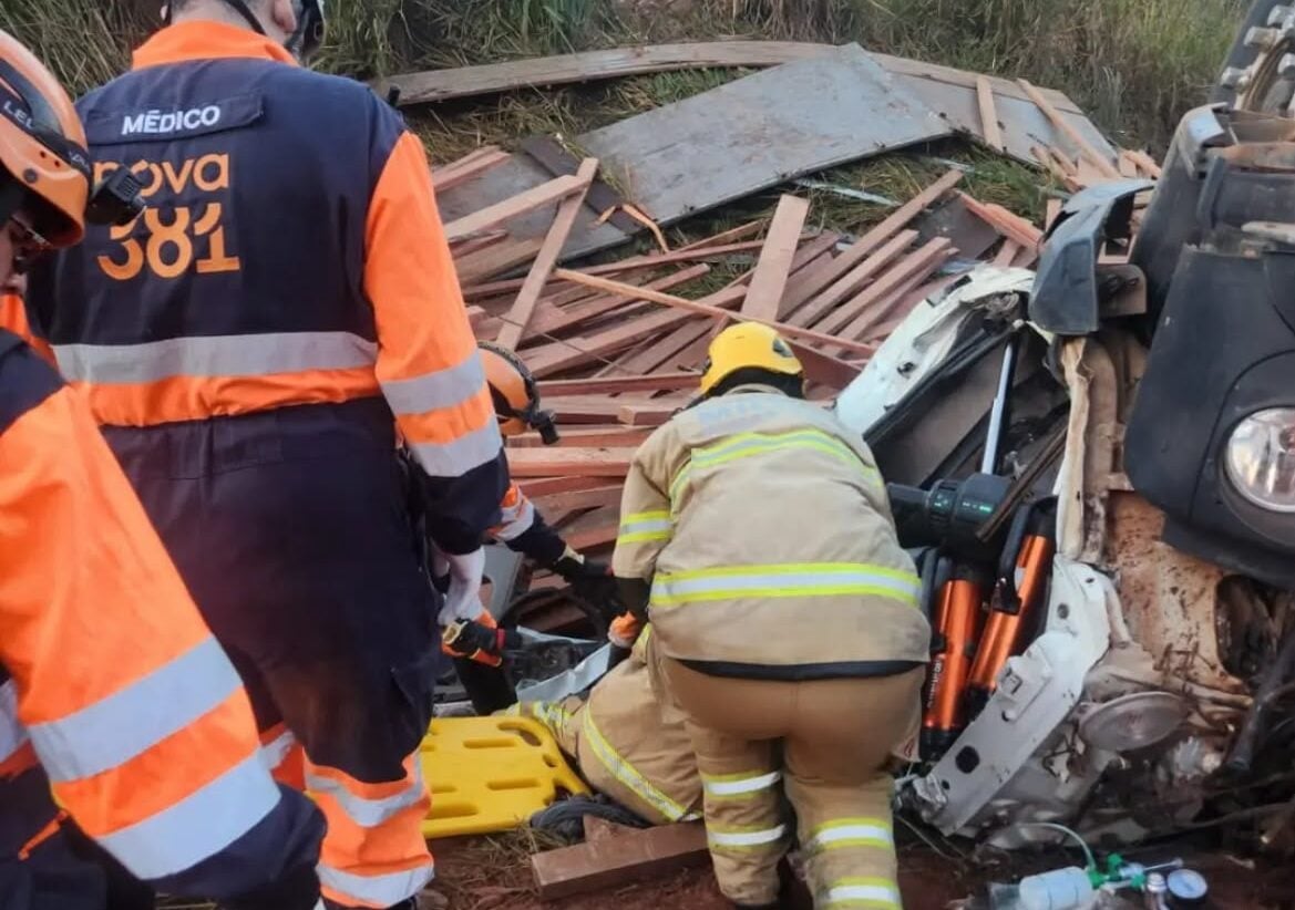 Caminhão carregado com madeira capota na BR-381 e deixa motorista preso às ferragens